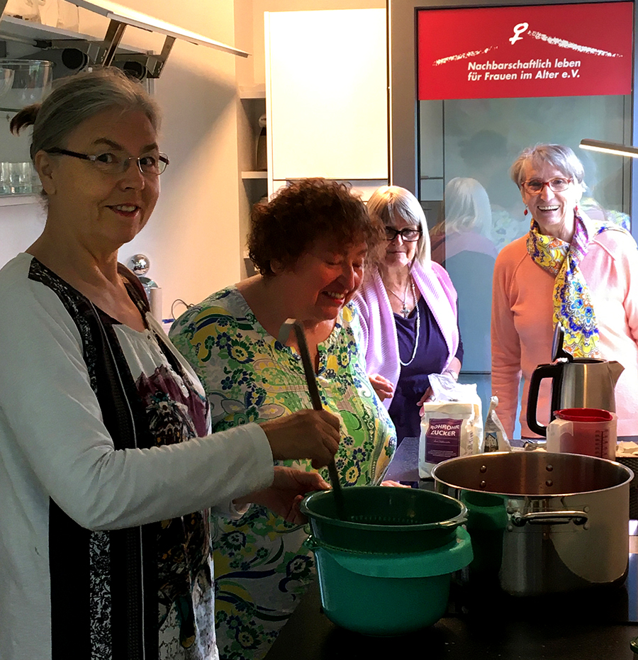 wg5: 3 Wohnfrauen kochen gemeinsam mit großem Kochtopf, eine Frau schaut bei der Fenstertüre herein